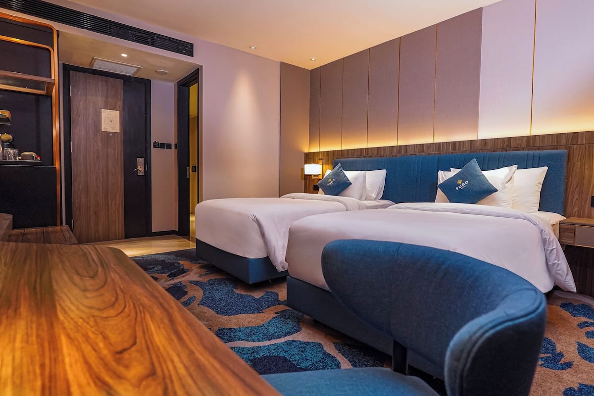 Ein Hotelzimmer mit zwei Betten, einem Holztisch und einem Nachttisch mit Lampe.