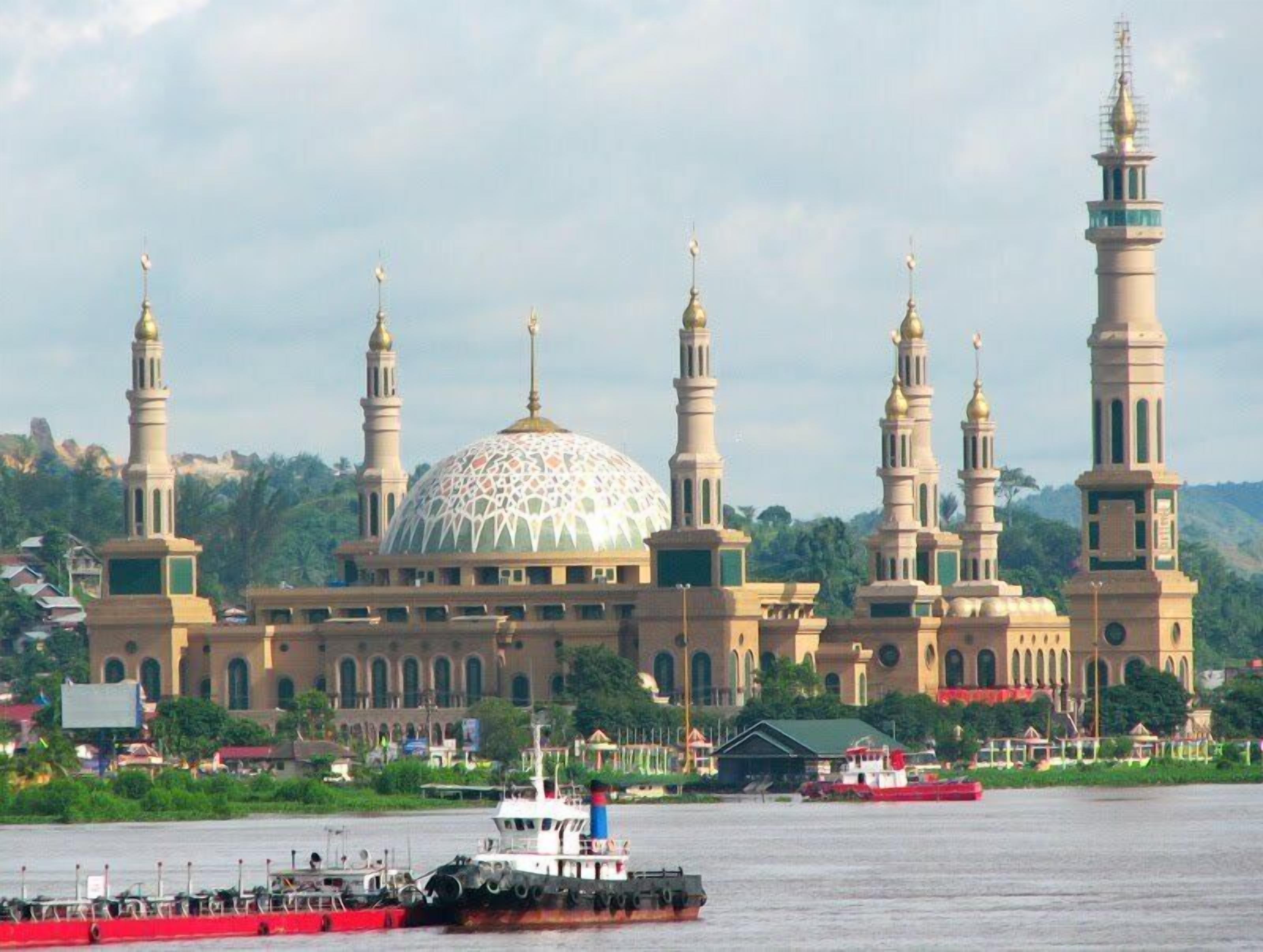 Una grande moschea con una cupola imponente e diversi minareti, affacciata su un corso d'acqua con imbarcazioni.