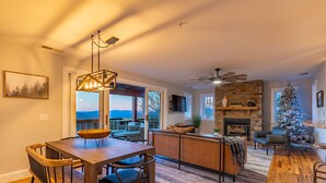 Amplia sala de estar con chimenea, una mesa de comedor con sillas y vistas al exterior.