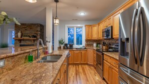 Una cocina moderna con encimeras de granito, electrodomésticos de acero inoxidable, armarios de madera y una pared de detalles de piedra.