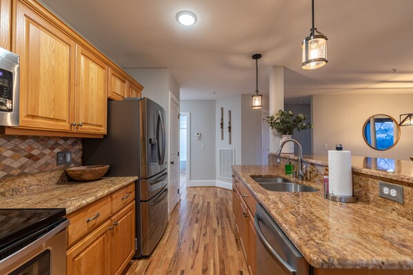 A kitchen with wooden cabinets, granite countertops, stainless steel appliances, and pendant lighting.