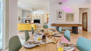 A dining area with a wooden table set for breakfast, chairs, and a neon sign on the wall.