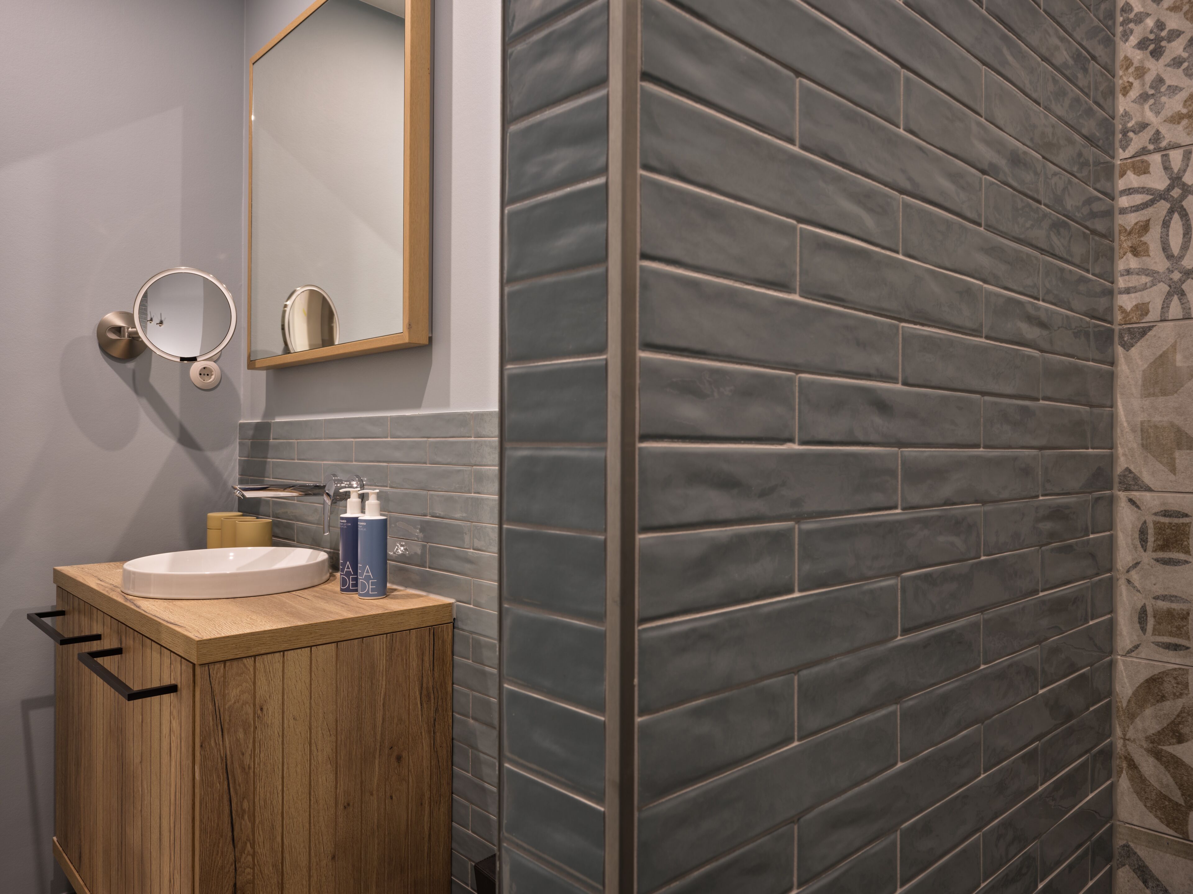 A bathroom with a wooden vanity, a round mirror, and a tiled wall.