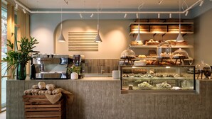 Una cafetería con mostrador de madera, máquina de café y vitrina con pasteles.