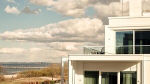 Un edificio moderno con techo plano, amplias ventanas y vista a un puente y al agua al fondo.