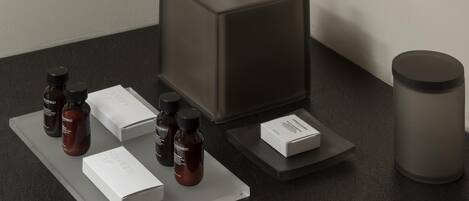 A bathroom counter with a tissue box, several bottles of shower gel, a box of shampoo, and a cylindrical container.