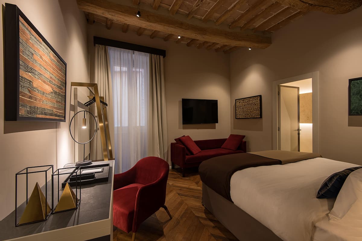 Moderni hotellihuone, jossa on suuri sänky, punainen nojatuoli, litteänäyttöinen televisio ja puinen katto.