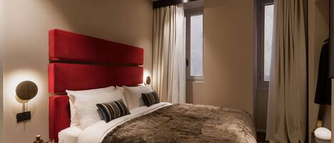 Un dormitorio moderno con una cama grande, cabecera roja, mesita de noche con lámpara y ventana con cortinas.