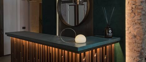 A modern reception desk with a wooden slat design, a round mirror, and pendant lighting.