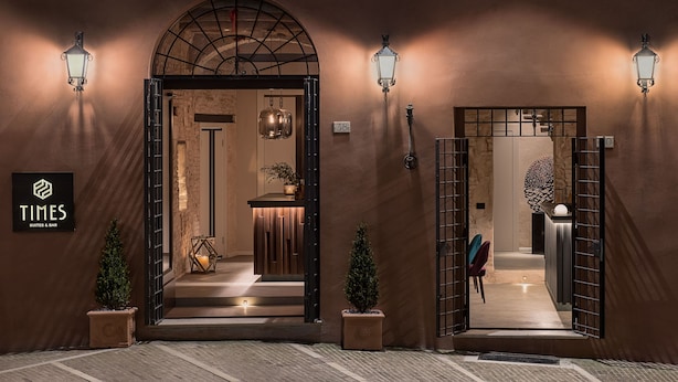 L’entrée d’un hôtel, avec une enseigne indiquant « TIMES SUITES & BAR », un escalier menant à l’intérieur et deux plantes en pot.