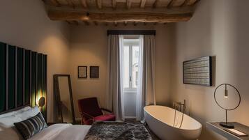 A bedroom with a large bed, a modern bathtub, a red chair, and a mirror.