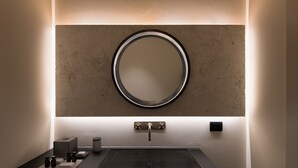 Une salle de bain moderne avec un miroir rond, un lavabo rectangulaire et une petite étagère contenant des articles de toilette.