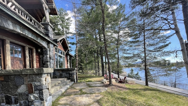A stone building with a stone staircase leading to a porch, surrounded by trees and a lake view. - Gorgeous lake views, walk to village, luxury chalet with 6,000+ sq (Lake Placid)