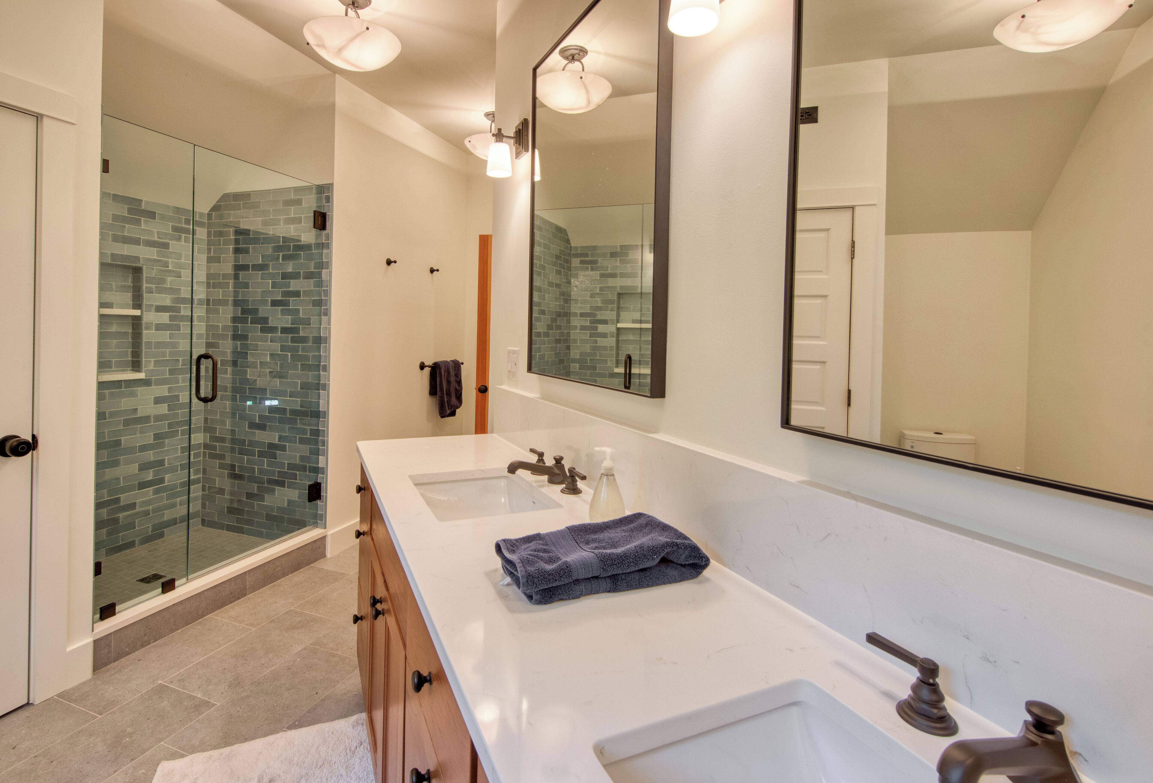 A modern bathroom with a glass shower enclosure, a large mirror, and a double sink vanity.