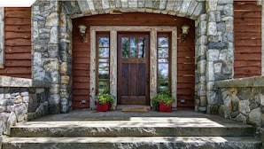 A log cabin with a stone archway, wooden door, and two potted plants on the steps. - Gorgeous lake views, walk to village, luxury chalet with 6,000+ sq (Lake Placid)