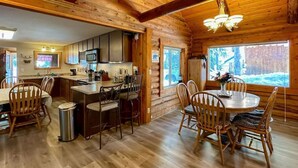 L’intérieur d’une cabane en rondins comprend une cuisine, un coin repas et de grandes fenêtres.
