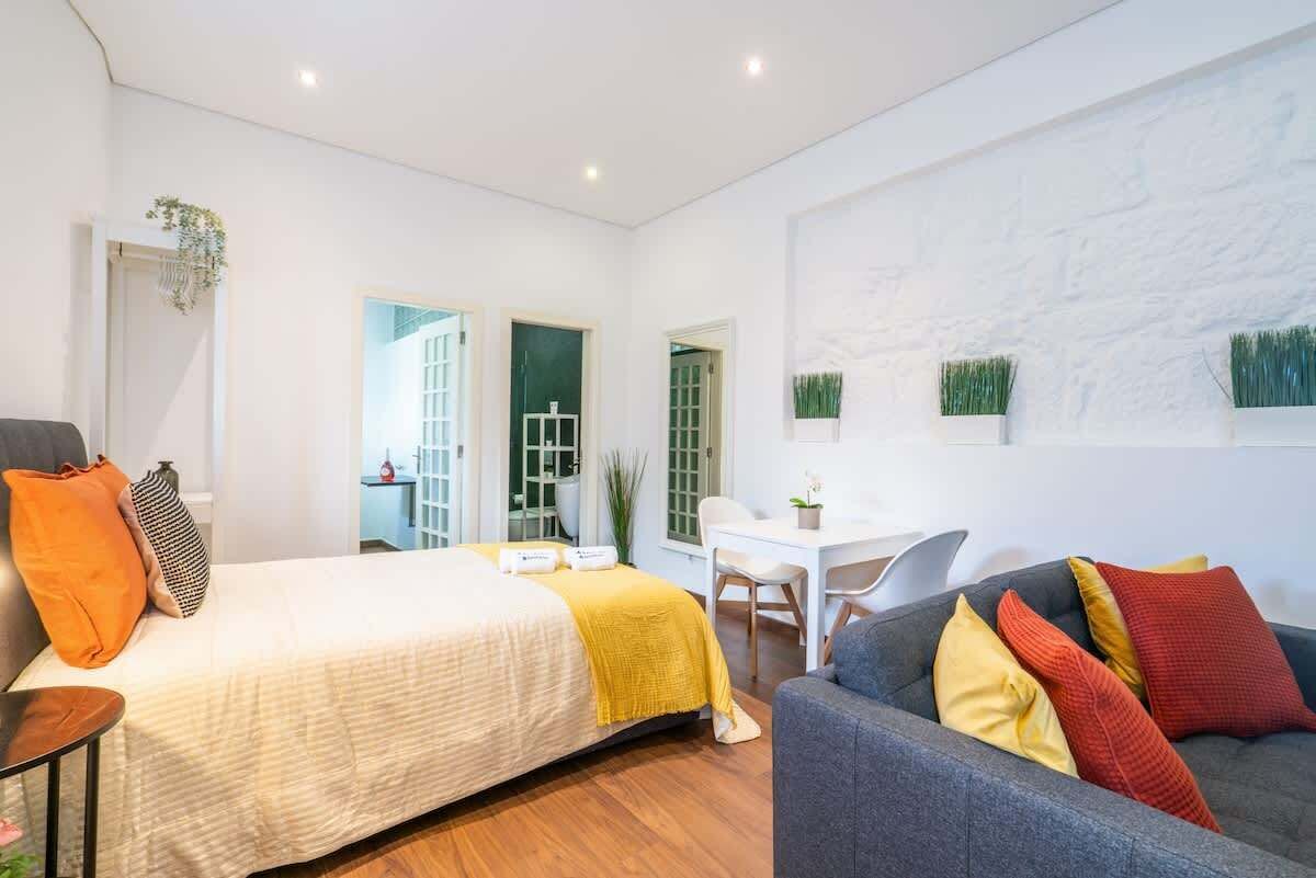 Une chambre d’hôtel moderne avec un grand lit, un canapé gris et un petit coin repas.