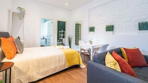Quarto de hotel moderno com uma cama grande, um sofá cinzento e uma pequena área de refeições.