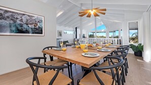 Un coin repas avec une table en bois dressée pour six personnes, entourée de chaises noires à assise tissée. Un grand tableau représentant un paysage naturel est accroché au mur.