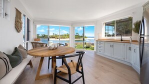 Een moderne keuken met uitzicht op het strand, een eethoek met een ronde tafel, en een zithoek met een bank.