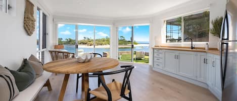 Una cocina moderna con vista a la playa, un comedor con mesa redonda y una sala de estar con sofá.