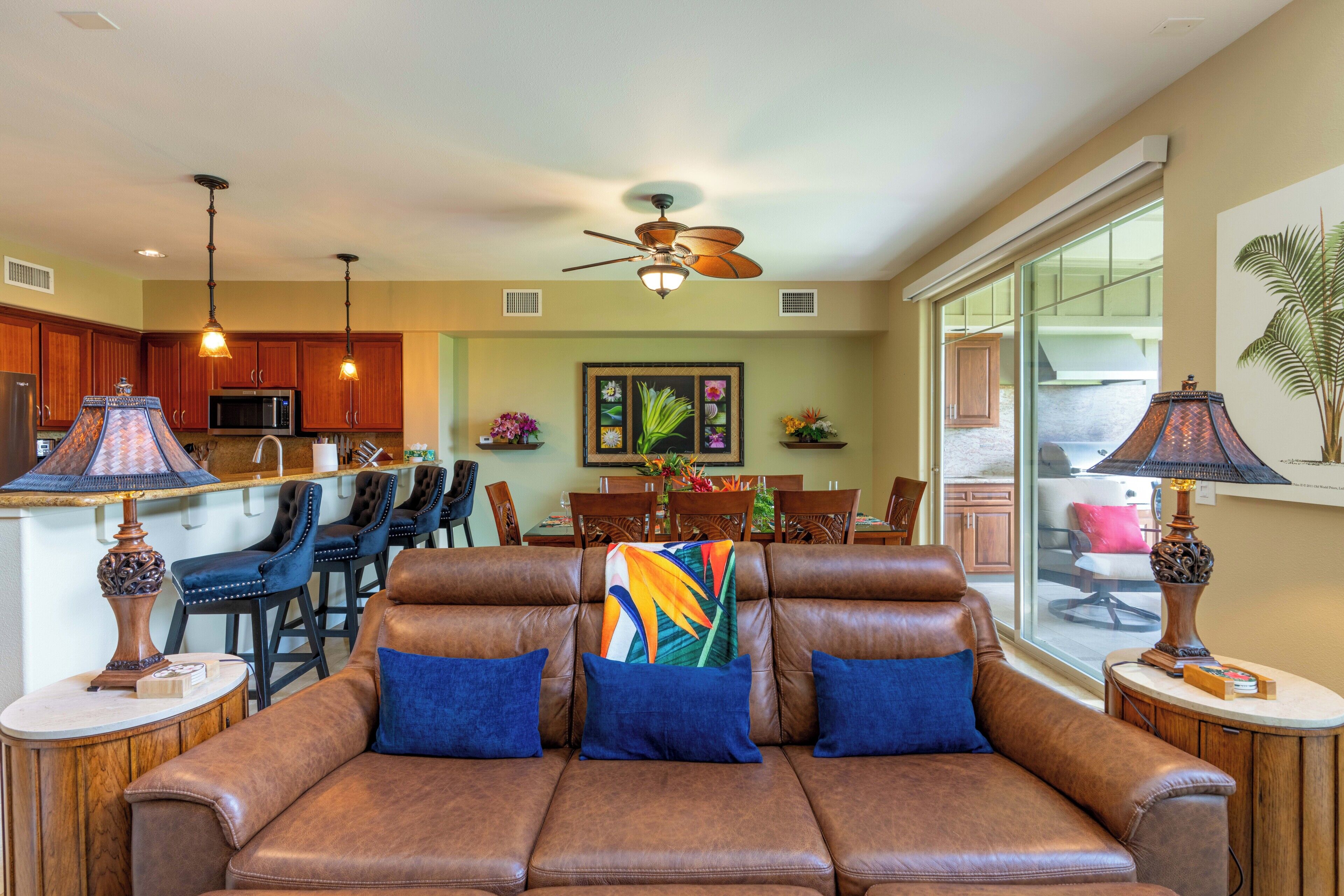 A living room with a sofa, a ceiling fan, and a dining area with chairs and a table.