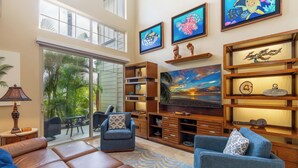 A spacious living room with a large TV, comfortable seating, and a view of the outdoors. - Gorgeous upgraded townhome + FREE Golf Cart! (Kamuela)