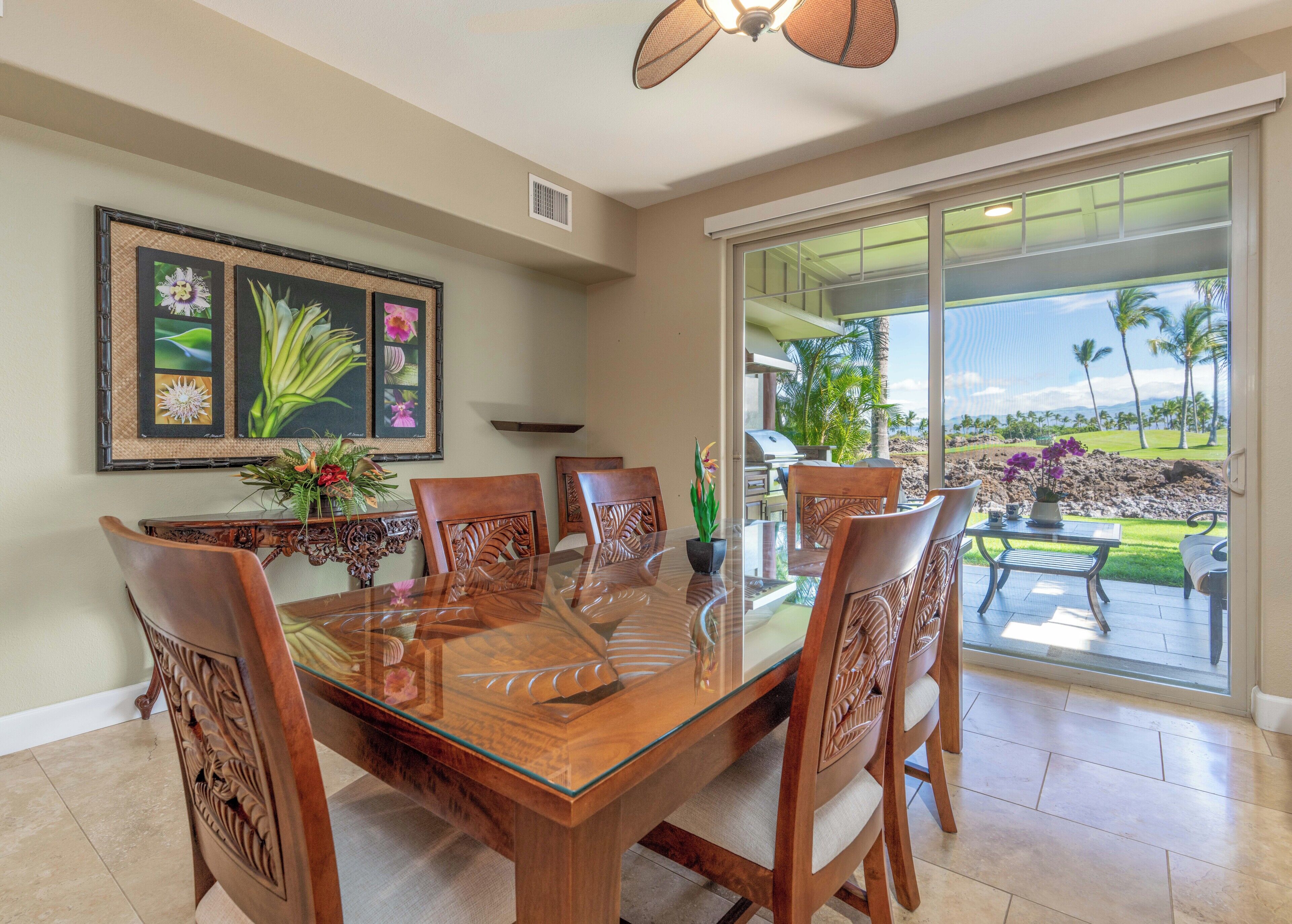 A dining area with a glass table, wooden chairs, and a view of the outdoors.