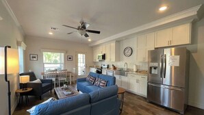Una cocina moderna con armarios blancos, un refrigerador de acero inoxidable y un área de comedor con sofá azul y una mesa.