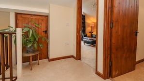 A hallway with wooden doors, a potted plant, and a sofa in the background. - The Coach House (Cheltenham)