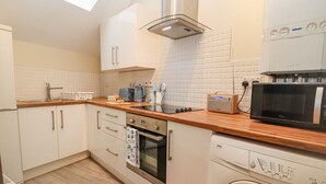 A modern kitchen with a built-in oven, microwave, and dishwasher. - The Coach House (Cheltenham)