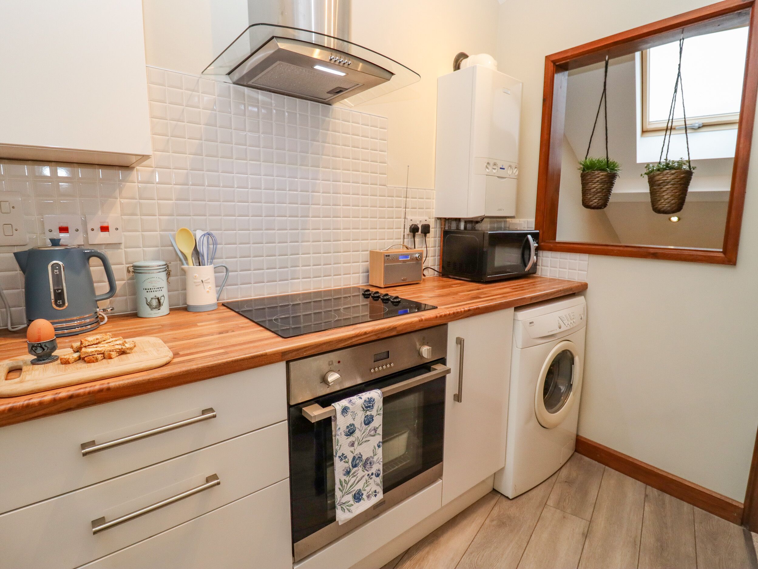 A compact kitchen with a stove, microwave, and oven, a washing machine, and a window with hanging plants.