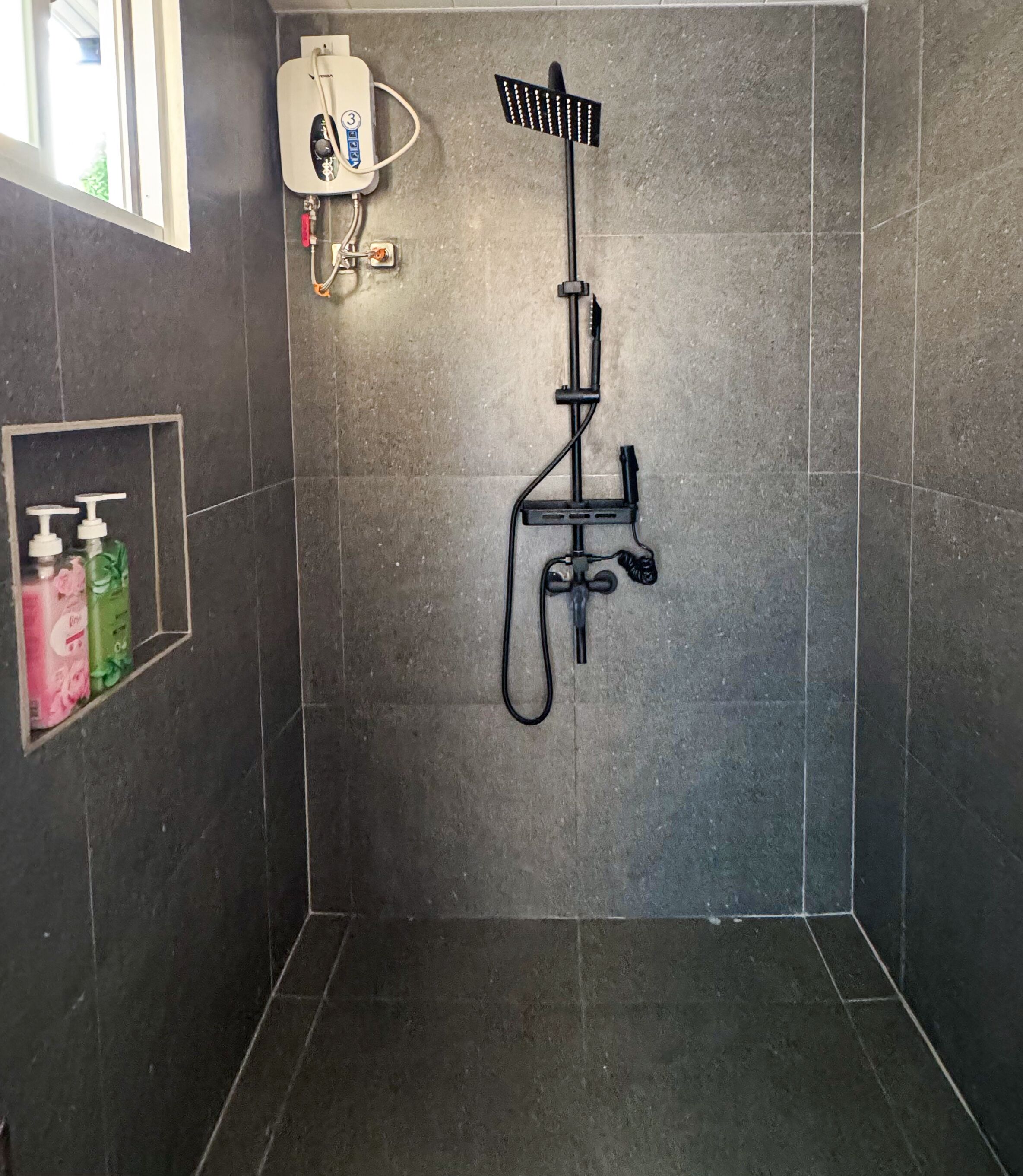 A shower area with a handheld showerhead, a wall-mounted faucet, and a small shelf with soap dispensers.