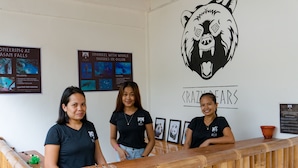 A reception desk with a wooden design, three individuals standing behind it, and wall posters about local wildlife. - Crazy Bears Hostel (Moalboal)