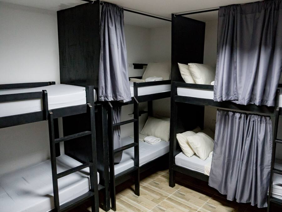 A dormitory-style room with bunk beds, each with a pillow and a blanket.