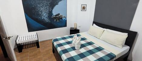 Un dormitorio con un mural grande de una ballena, una cama con colcha a cuadros y un pequeño banco junto a la puerta.