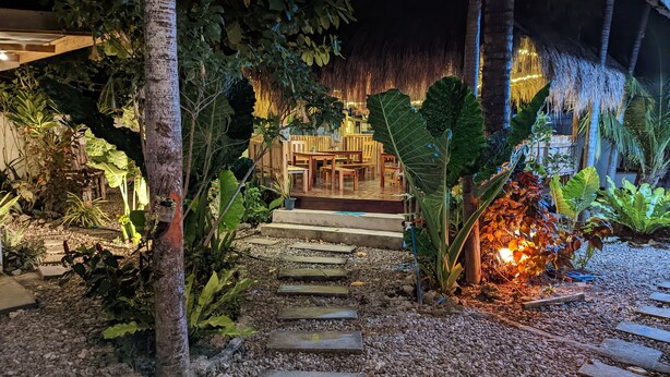 A tropical garden pathway leading to a wooden deck with a thatched roof. - Crazy Bears Hostel (Moalboal)
