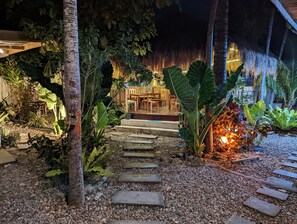 A tropical garden pathway leading to a wooden deck with a thatched roof. - Crazy Bears Hostel (Moalboal)
