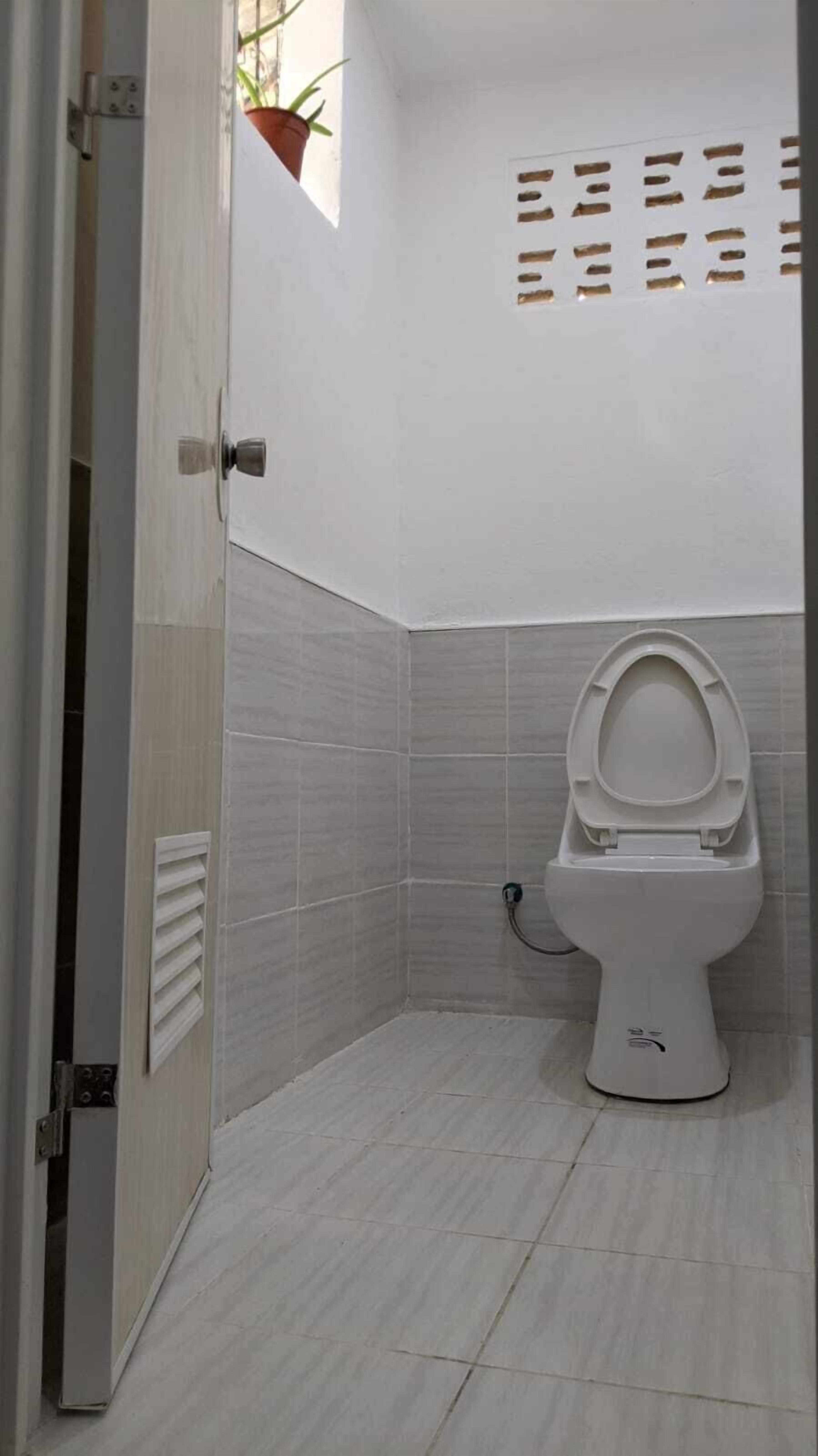 Een kleine, moderne badkamer met toilet, betegelde wanden en een ventilatieopening aan de linkerkant.