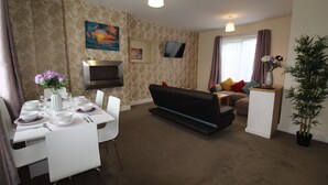 A living room with a dining table set for four, a black sofa, a flat-screen TV mounted on the wall, and a potted plant. - Chadwick House (Sheffield)