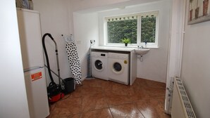 A laundry room with a washing machine, dryer, sink, and a window with a view of greenery. - Chadwick House (Sheffield)