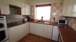 A kitchen with white cabinets, a tiled backsplash, a window with a red curtain, and a microwave. - Chadwick House (Sheffield)