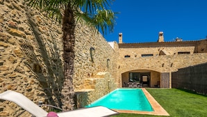 Un bâtiment en pierre avec une piscine, un palmier et un ciel bleu azur.
