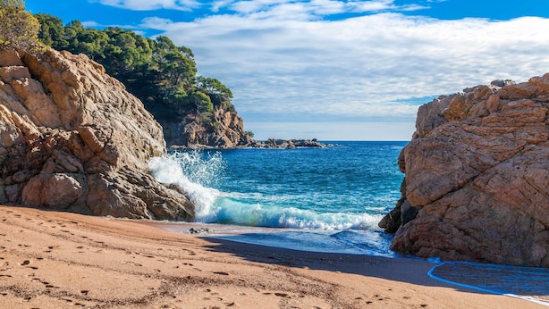 Une plage bordée de falaises rocheuses et aux eaux d’un bleu limpide.