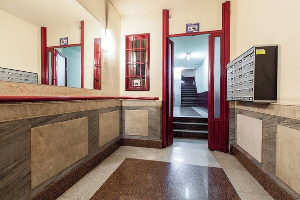 A hotel lobby with a marble floor, red-framed doors, a staircase, and a filing cabinet.