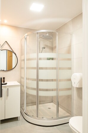 Une salle de bain moderne avec une douche à parois de verre, un miroir rond et des toilettes.