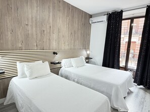 Une chambre d’hôtel avec deux lits, une tête de lit en bois, un appareil de climatisation et une vue sur un balcon.