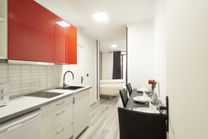 Une cuisine compacte au design moderne, dotée d’un plan de travail blanc, d’un meuble rouge et d’un grill encastré.