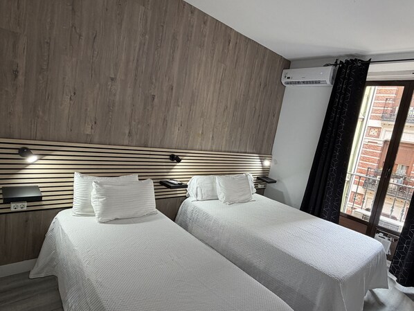Une chambre d’hôtel avec deux lits, une tête de lit en bois, des lampes de chevet et un appareil de climatisation.