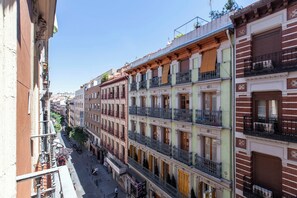 A row of multi-story buildings with balconies, a street in the foreground, and a clear sky.
